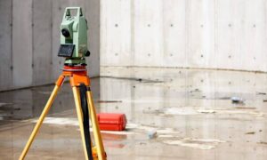 Total station surveying equipment set up on wet concrete after heavy rain, illustrating flood elevation measurement and drainage assessment.
