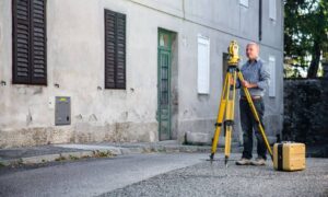 Licensed land surveyor measuring a home's height to prepare an elevation certificate after heavy rain