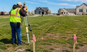Surveyor conducting a boundary survey on a desert property with stakes and measuring equipment marking a straight property line across open land