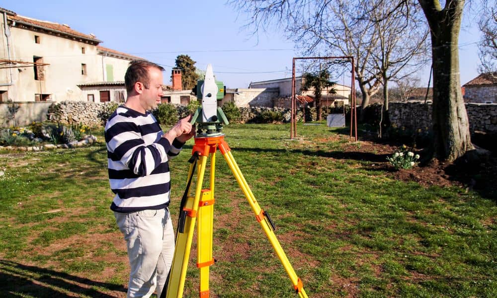 A land surveyor using a total station to measure a residential property during a property survey
