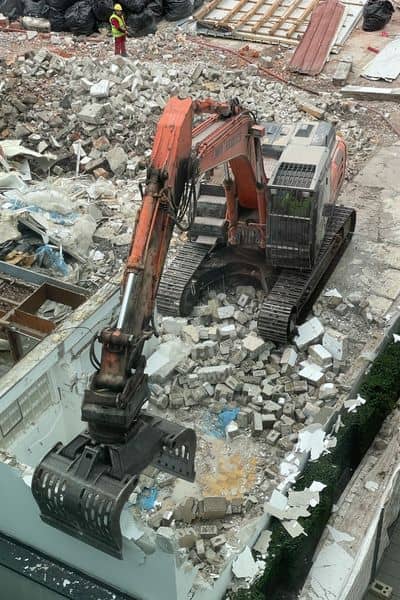 Excavator breaking and removing concrete during construction rework after field misplacement identified during a construction survey on a busy job site